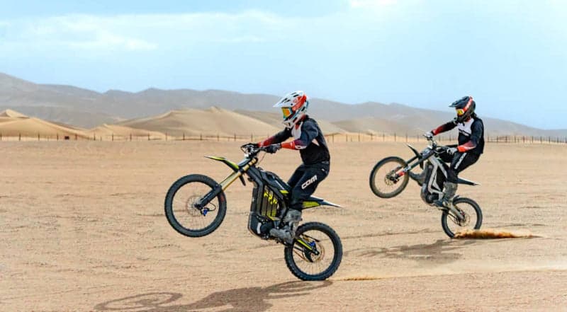 Two riders doing wheelies on electric dirt bikes in the desert